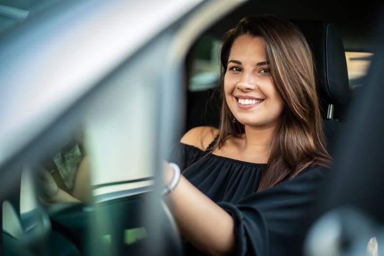 A smiling woman behind the steering wheel of a car.