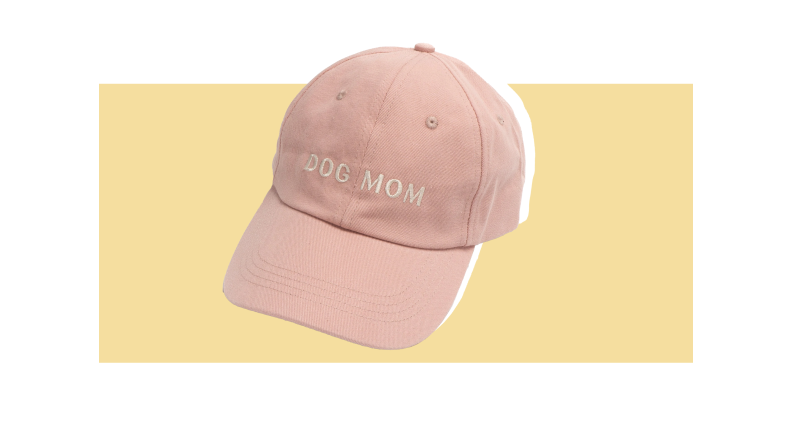 A pink hat that says "Dog Mom" against a light gold background.