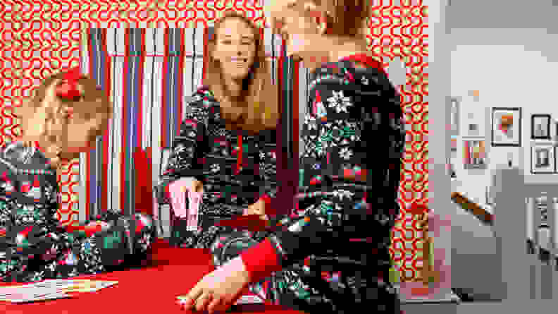 A mom and two children, all wearing matching Christmas pajamas, playing a card game.