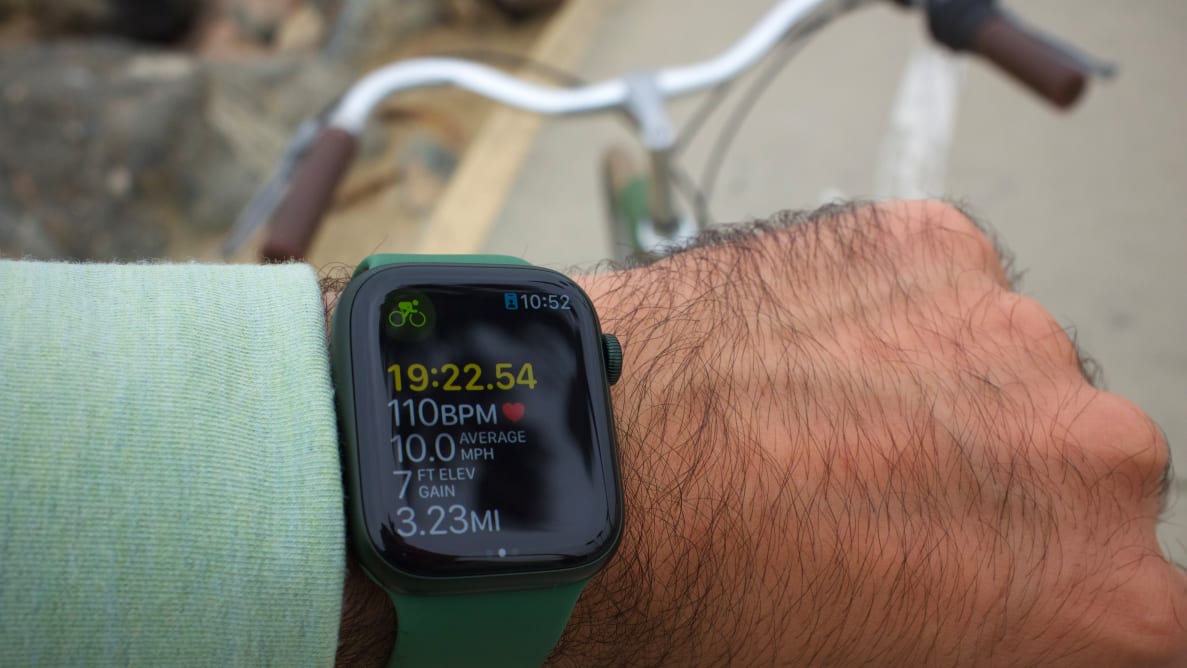 A close-up of the Apple Watch Series 7, in green, showing its cycling workout tracking, with the handlebars of a bicycle in the background.