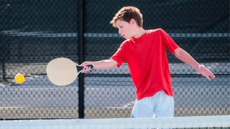 A child plays pickleball on a court.