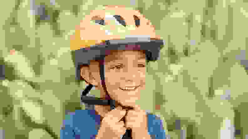 A young boy fastens his orange bike helmet.