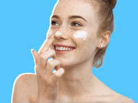Person smiling while applying facial cream to nose and cheeks.