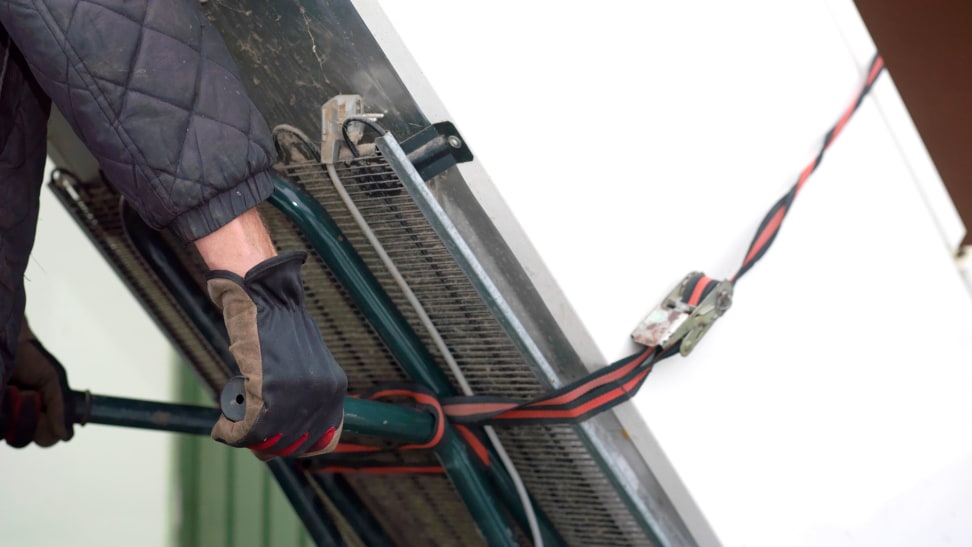 A person with work gloves is moving an old refrigerator secured to a dolly.