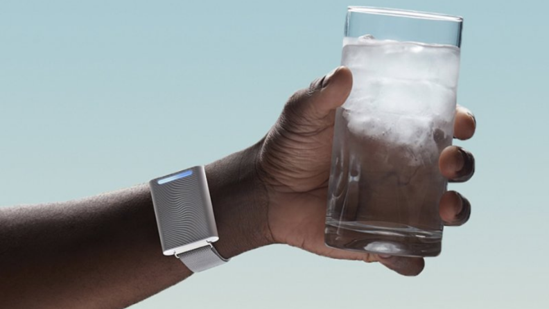 A person clutches a glass of water while wearing an Embr Wave Bracelet.