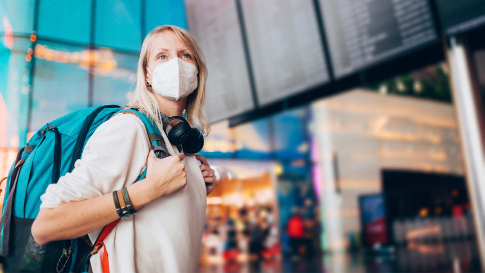 A person wearing a face mask, backpack, and headphones in an airport.
