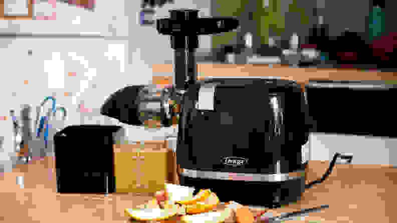 Omega H3000D Cold Press 365 sits on a counter in a kitchen with citrus peels in front of it and a full cup of orange juice.