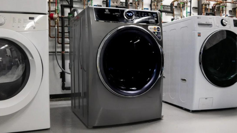 A silver washing machine stands between two white ones