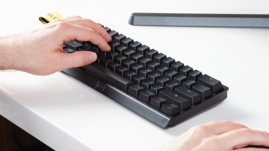 Close up angled shot of the Wooting 60he keyboard on a white desk with a hand on it