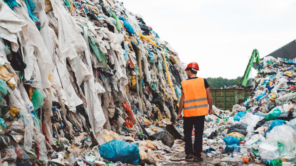 man in landfill surrounded by used clothing