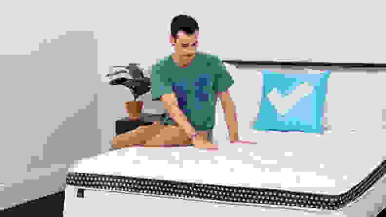 Person sitting on top of a WinkBed hybrid mattress and using hands to feel bed's material.