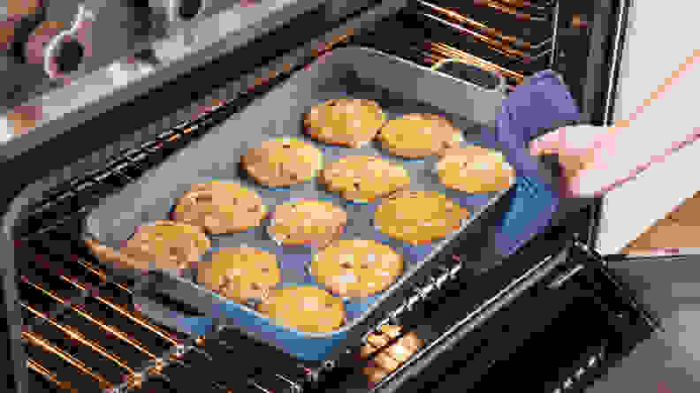 A hand pulls an Our Place tray of cookies out of an oven.