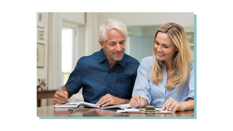 Elderly couple sitting at table while discussing finances and writing down notes with bills.