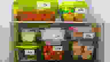 Several labeled containers of food stacked in a fridge