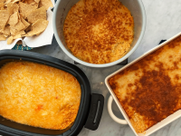 A bowl of tortilla chips and three pans of buffalo chicken dip laid out on a marble counter.