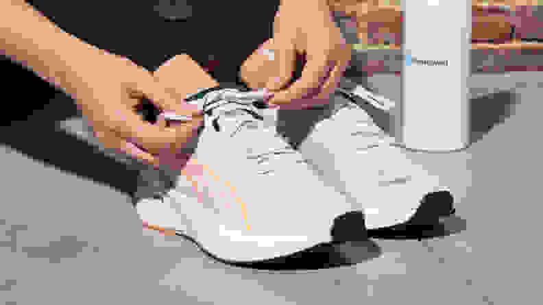 A person ties the laces on a pair of white running shoes outside.