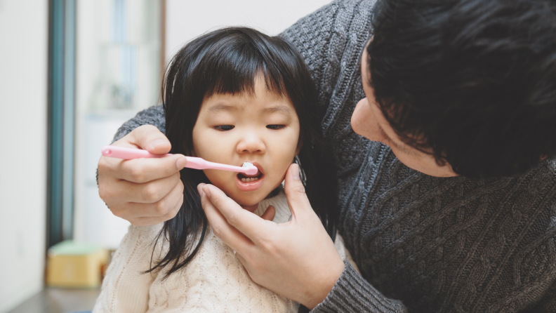 Dad brushing little girl's teeth