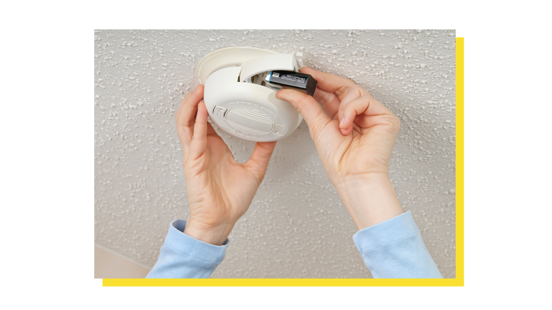 Person installing battery into smoke device mounted on ceiling.