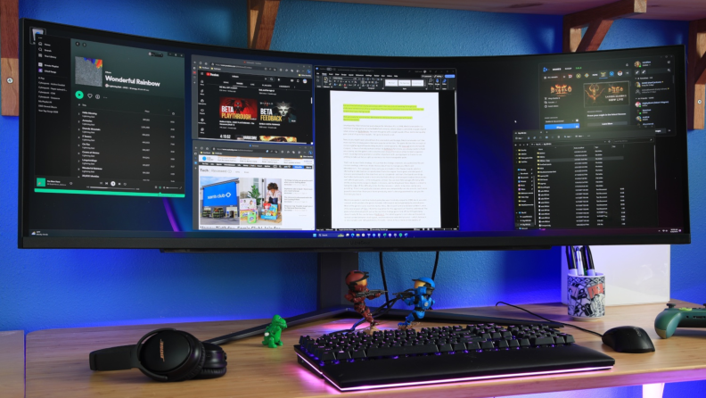 An ultrawide monitor with multiple tabs open sits on a desk with keyboard and peripherals.