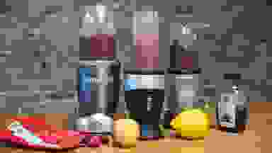 Three personal blenders with purple smoothies against a brick wall