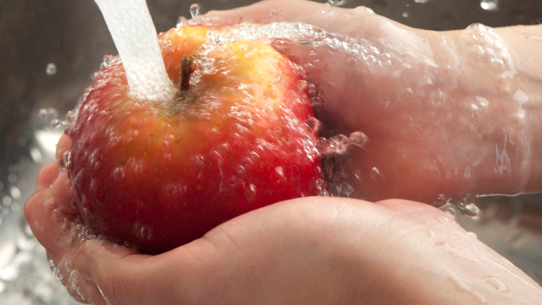A person washes an apple under a running faucet.
