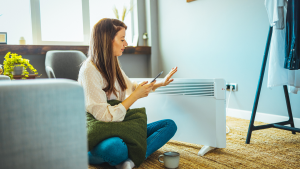 Person sitting in front of space heater while holding hand up to moderate heat.