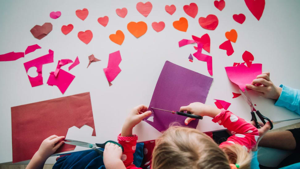 Three children cut out hearts for a Valentine's Day crafts.