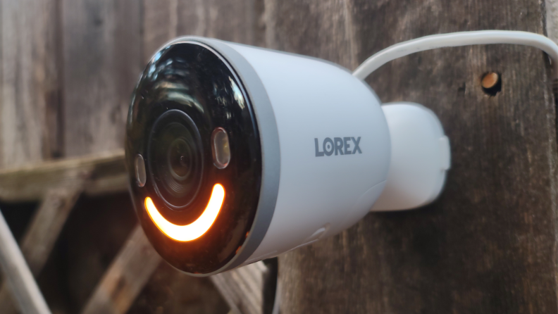 Lorex 4K Spotlight mounted on wooden fence outdoors with orange LED light.