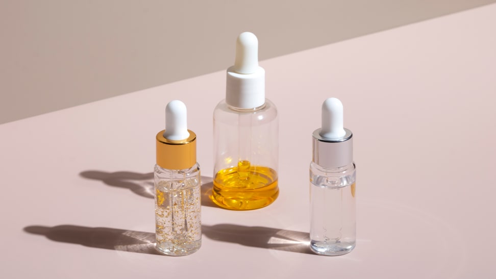 Three serum bottles with liquids in them capped with droppers stand on a light pink background.