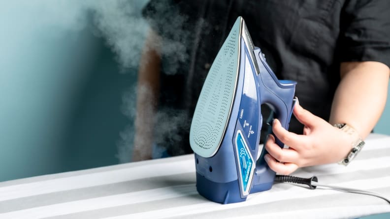 A person using the steam function on an iron to release a puff of steam.