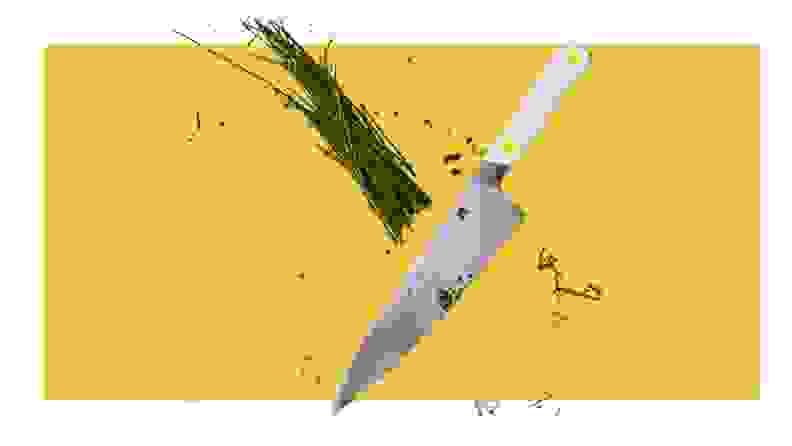 Chef's knife slicing through chives on a yellow background