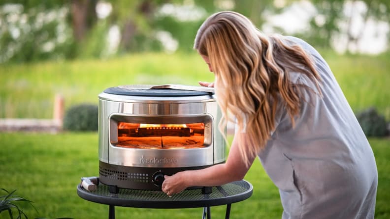 Person crouches down outdoors in front of the Solo Pi Prime to adjust temperature settings with knob.