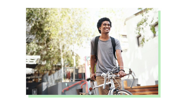 A smiling young student dressed casually with a bicycle.