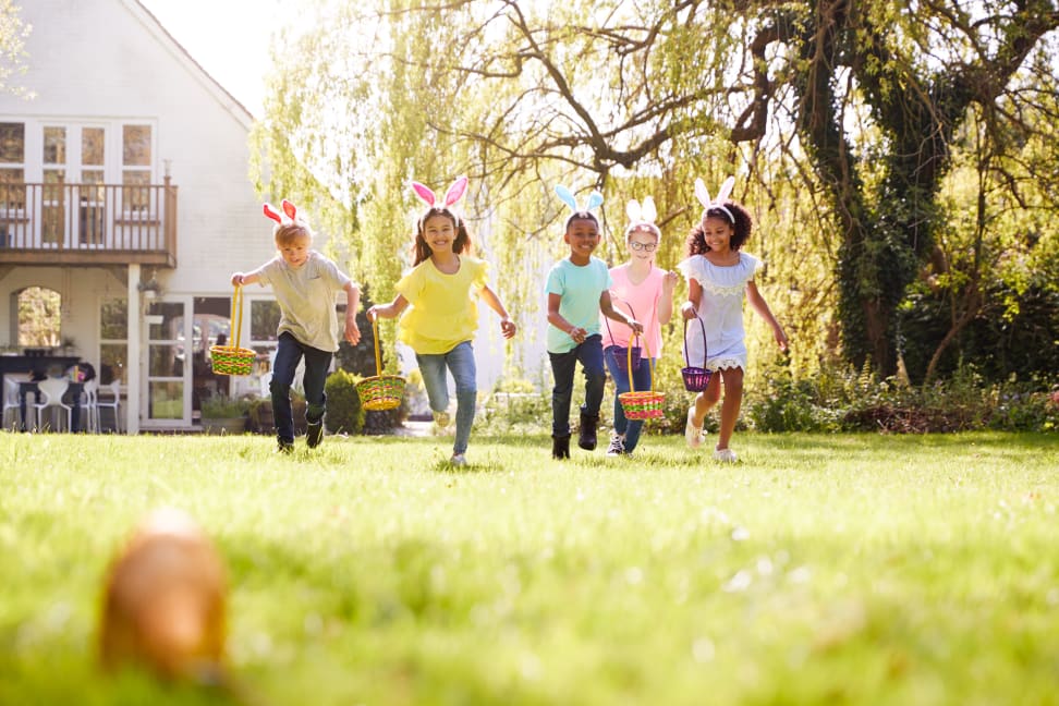Five children run towards an Easter egg, baskets in hand and bunny ears on.