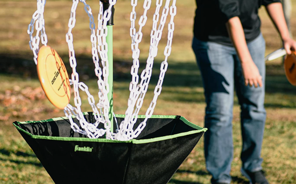 Photo of a young model in a black polo enjoying the Franklin Sports Disc Golf Basket.