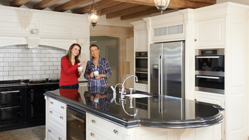 Two women standing in kitchen smiling while admiring their surroundings.