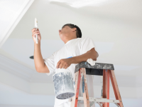 Person on ladder painting the ceiling white with a brush