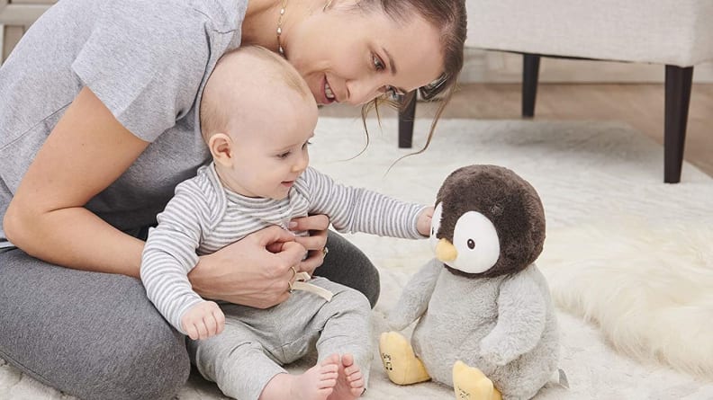 Mother and baby sitting on carpeted floor while playing with stuffed penguin.