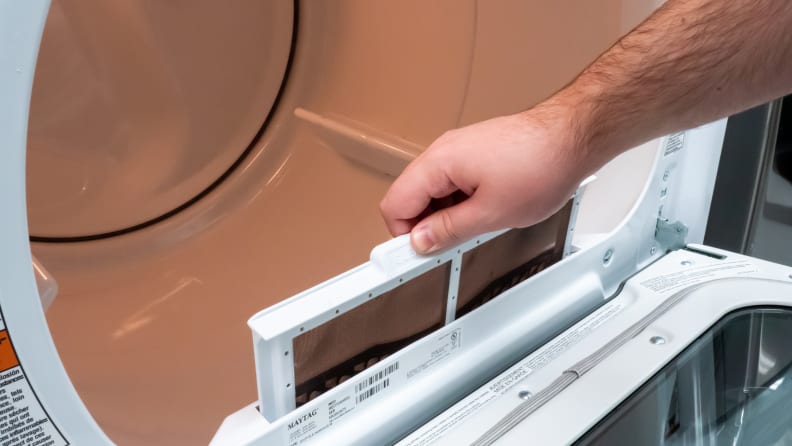 A close-up of a hand reaching into frame to lift up the Maytag MED7230HW dryer's lint trap.