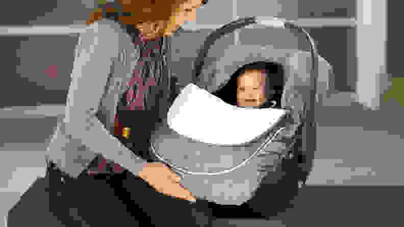 A baby in a car seat that has a cover on it.