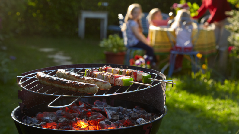 Skewers cooking on a charcoal grill in a sunny backyard.