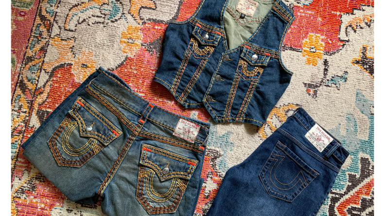 Two pairs of jeans and a denim vest with bold stitching on a patterned rug.