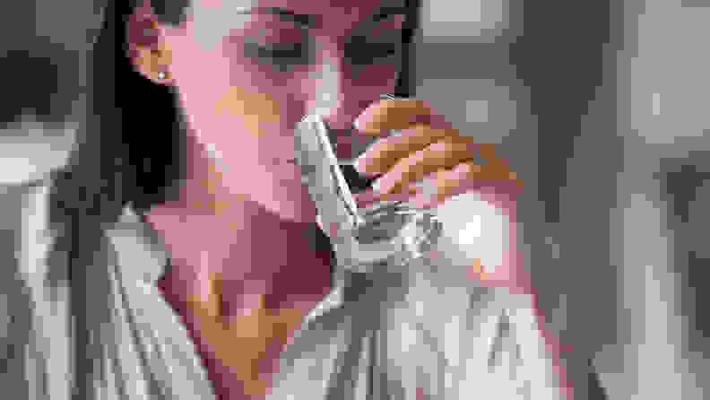 A woman drinks from a glass of water.