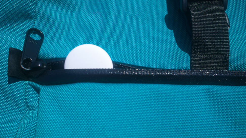 An Apple AirTag resting inside the zipped up pocket of a blue backpack.