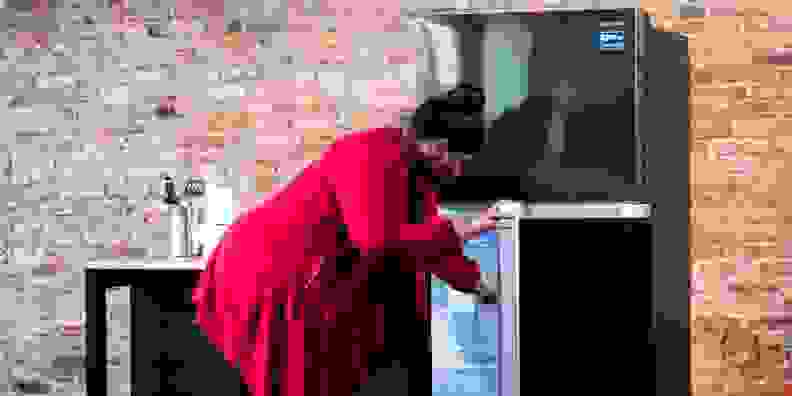 A woman in a red sweater looks into a refrigerator