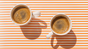 两个白色的浓缩咖啡杯，里面装满了浓缩咖啡，背景是橙色和白色的条纹。