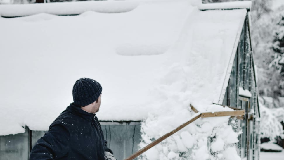 A man clears snow with a roof rake.