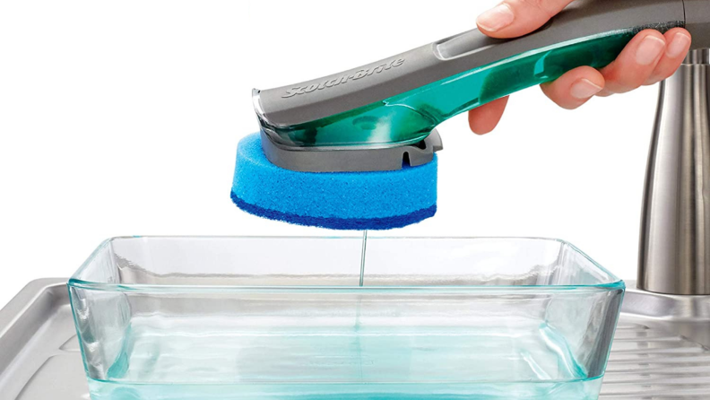 A person washes a dish with a Scotch-Brite dish wand.