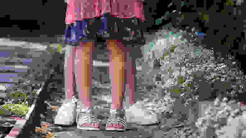 A pair of children's feet wearing silver sandals in front of a pair of children's feet wearing white tennis shoes.