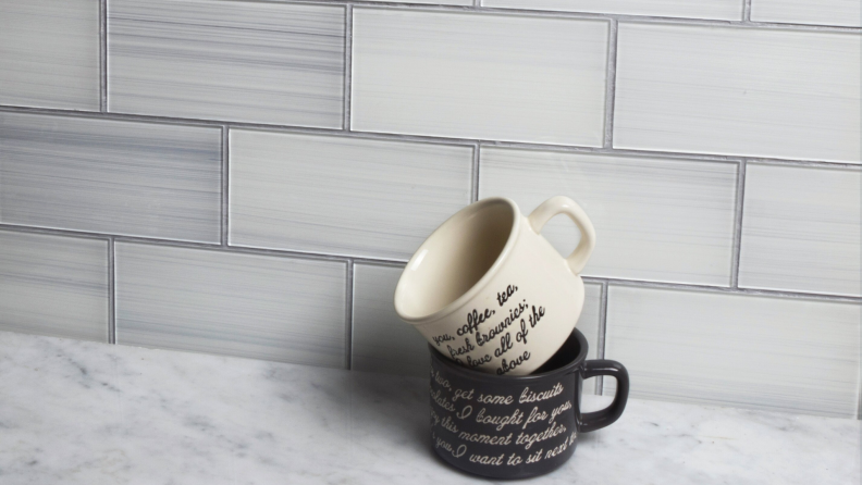 Two mugs stacked on top of each other against peel and stick tile, on top of marble countertop